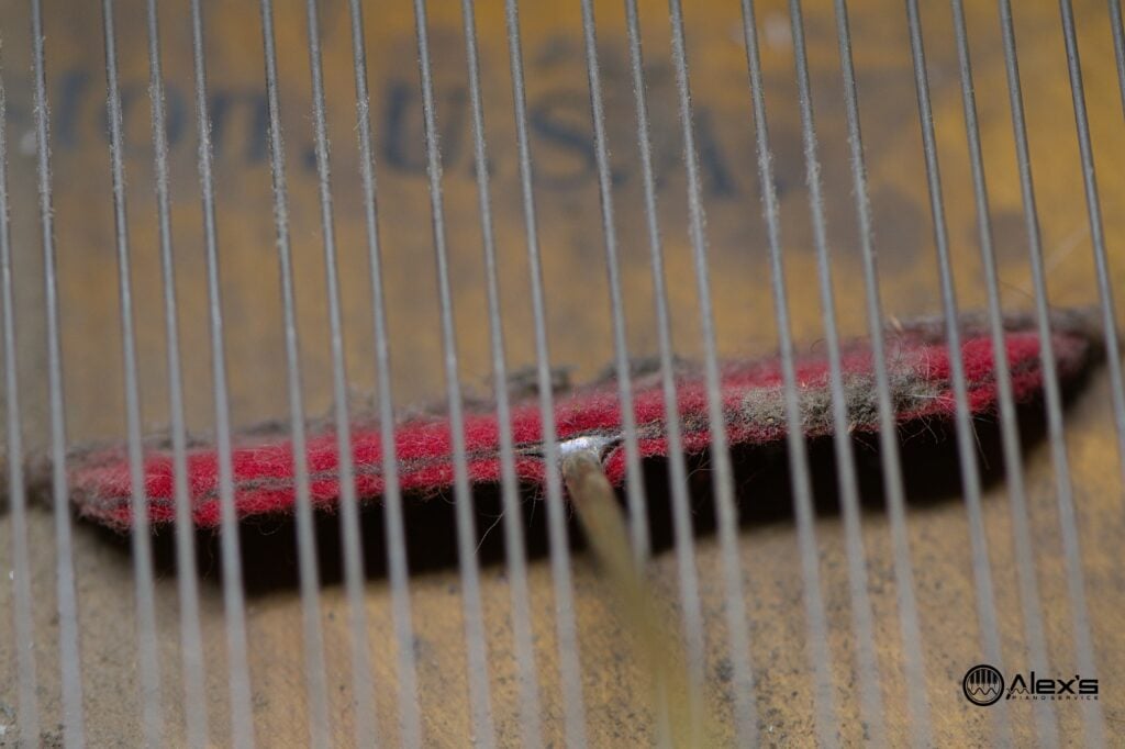 A Spurlock Soundboard Squeegie cleaning dust from underneath thing strings in a grand piano.